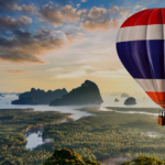 A hot air balloon flying in the colour of Thailand's flag flying above a land crossed by the river in Thailand